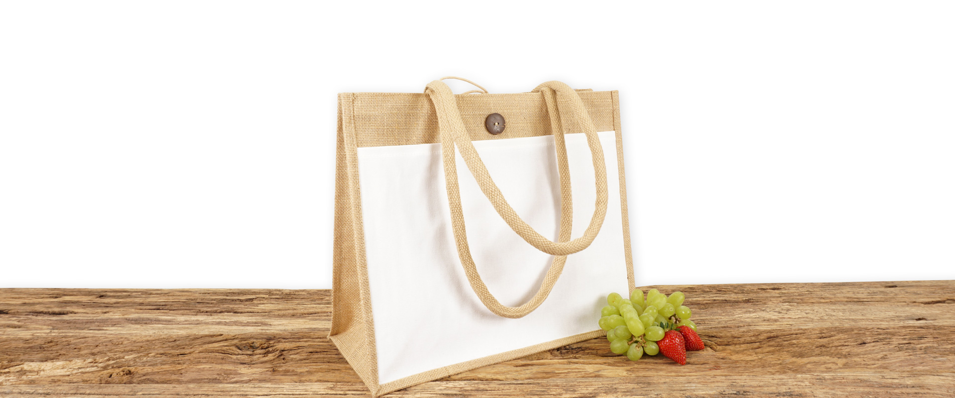 Einkaufstasche aus Jute mit weißer Fronttasche zum Bedrucken, naturfarben mit Seiten-Bodenfalte, mittelgroß und mit langen Tragegriffen auf Holz.