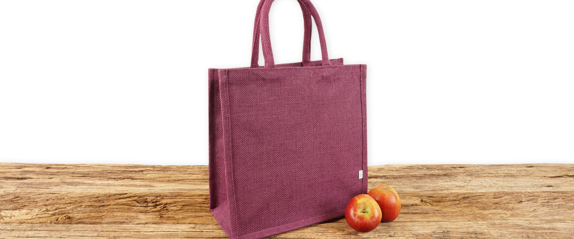Einkaufstasche aus Jute zum Bedrucken, auberginefarben mit Seiten-Bodenfalte, klein und mit kurzen Tragegriffen auf Holz.
