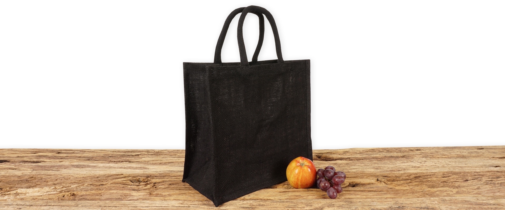 Einkaufstasche aus Jute zum Bedrucken, schwarz mit Seiten-Bodenfalte, klein und mit kurzen Tragegriffen auf Holz.