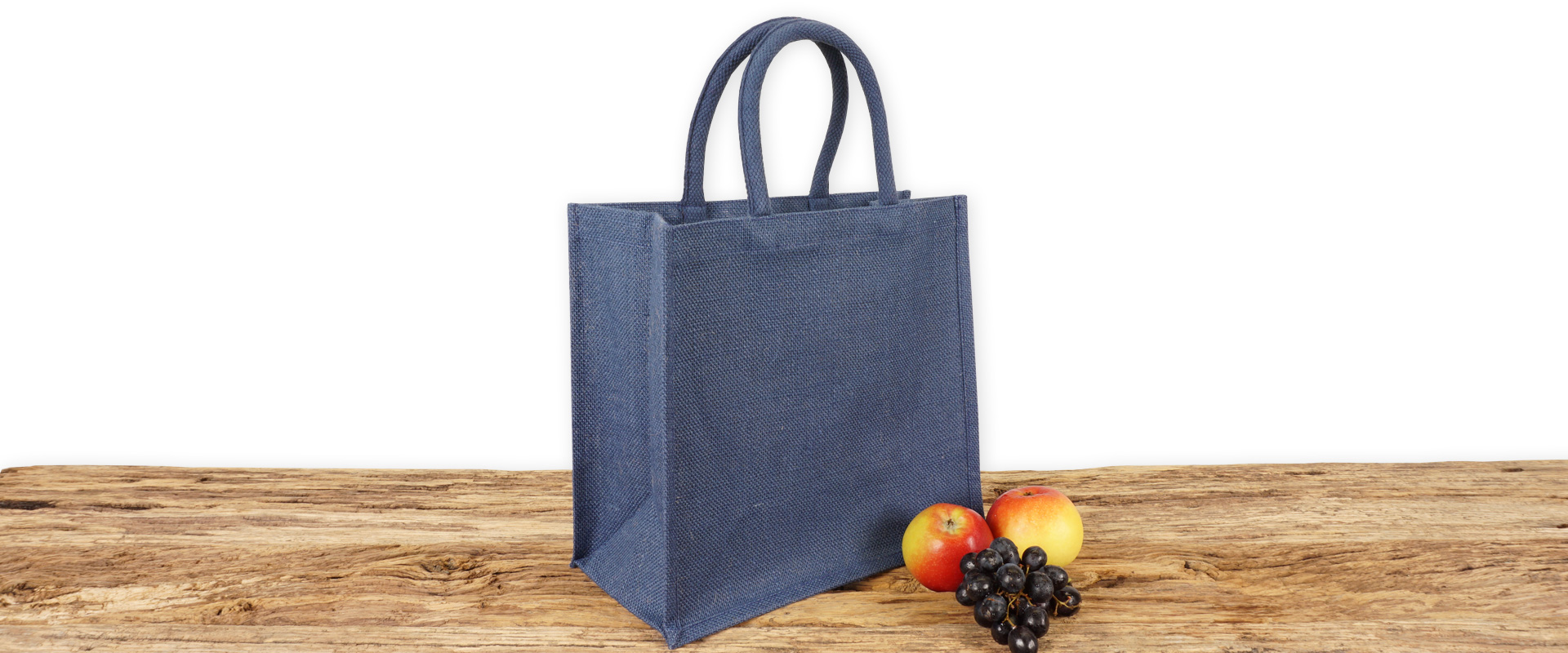 Einkaufstasche aus Jute zum Bedrucken, dunkelblau mit Seiten-Bodenfalte, klein und mit kurzen Tragegriffen auf Holz.