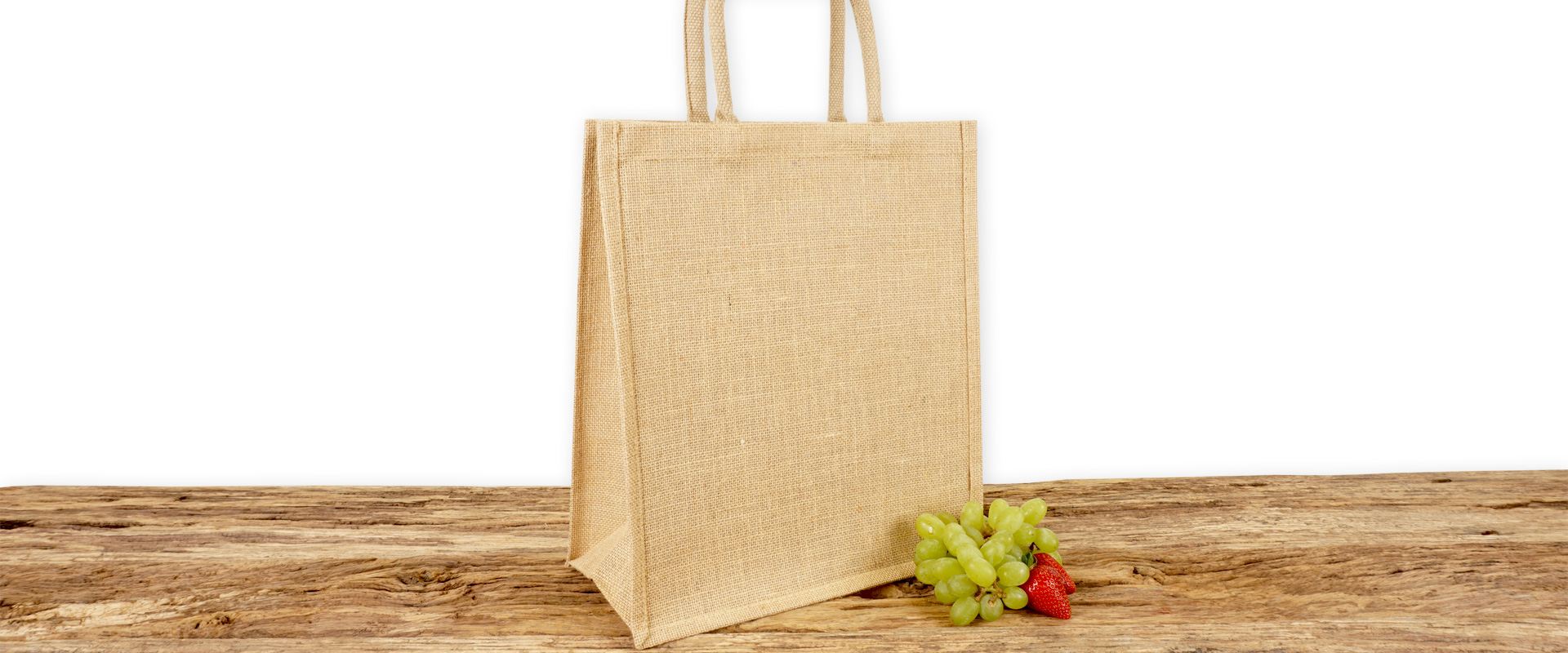 Einkaufstasche aus Jute zum Bedrucken für Handel und Gewerbe, in Natur mit Seiten-Bodenfalte, A4 Hochformat und mit kurzen Tragegriffen auf Holz.