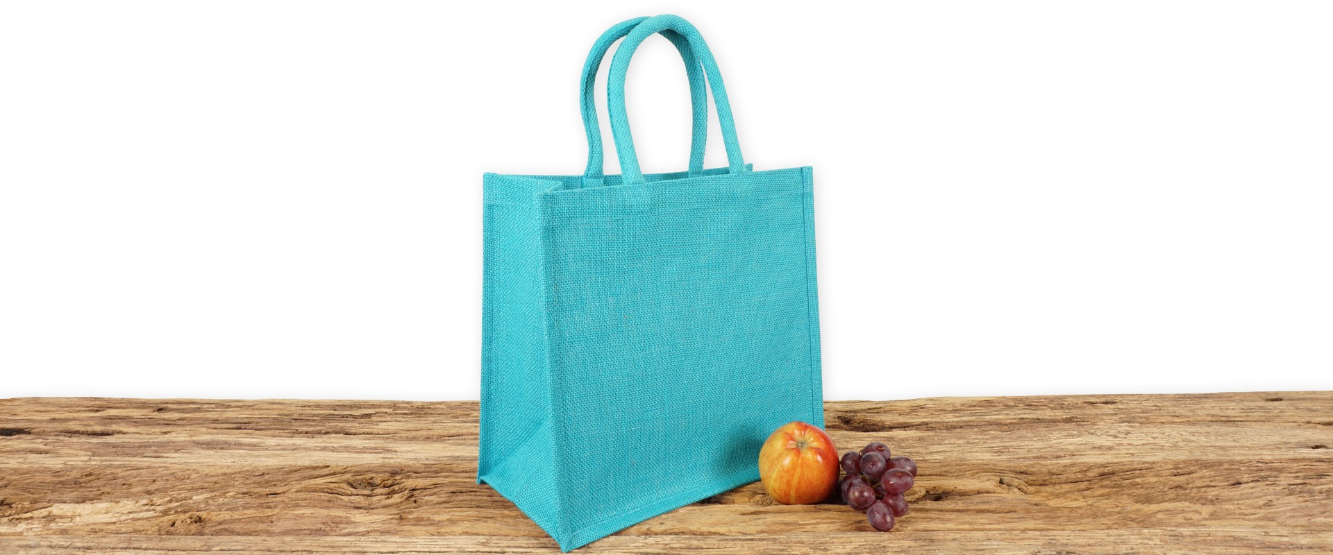 Einkaufstasche aus Jute zum Bedrucken für Handel und Gewerbe in Hellblau mit Seiten-Bodenfalte, klein und mit kurzen Tragegriffen auf Holz.